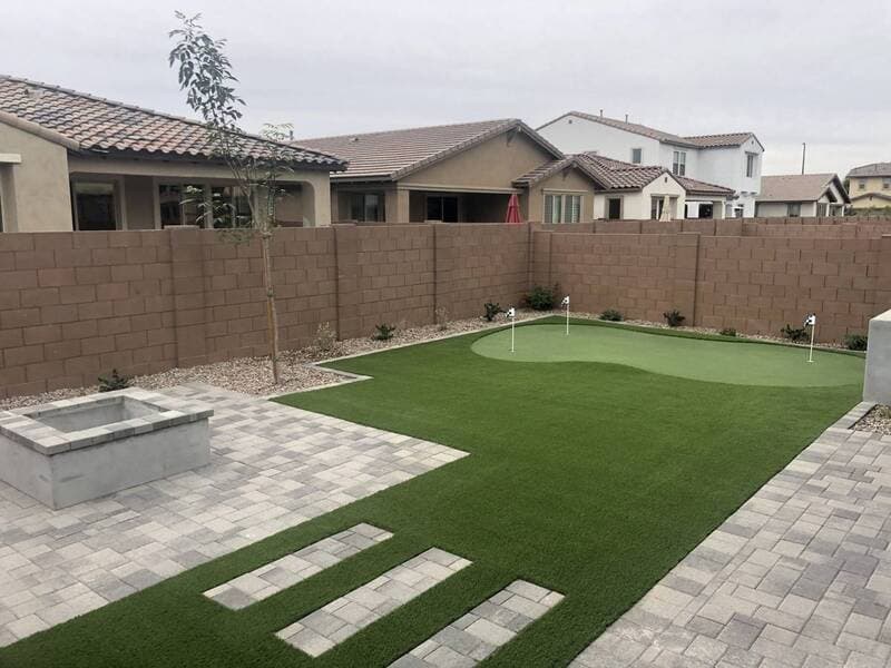 Modern backyard featuring synthetic grass, a putting green, and stone fire pit.