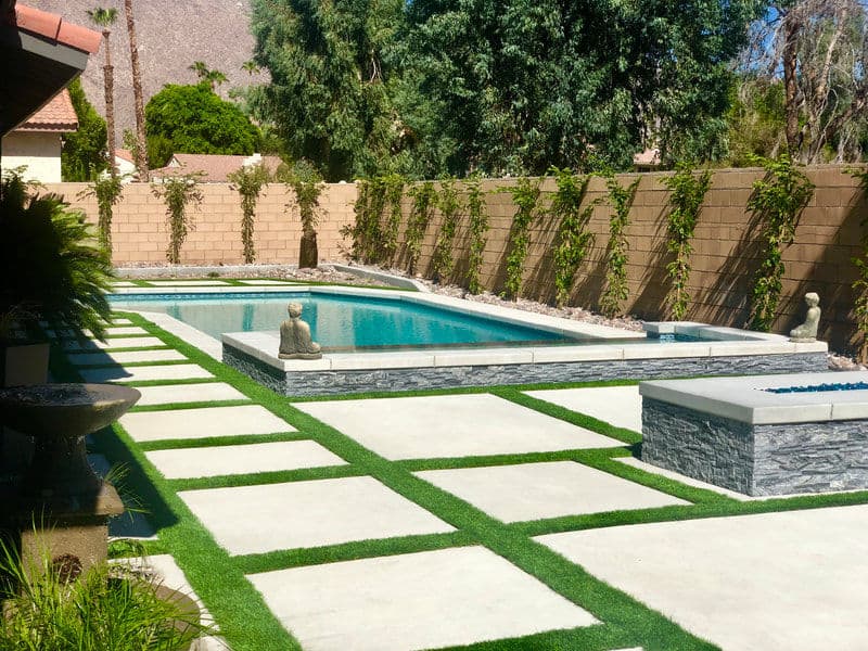 Modern backyard with a pool, stone sculptures, and landscaped paths featuring artificial grass.