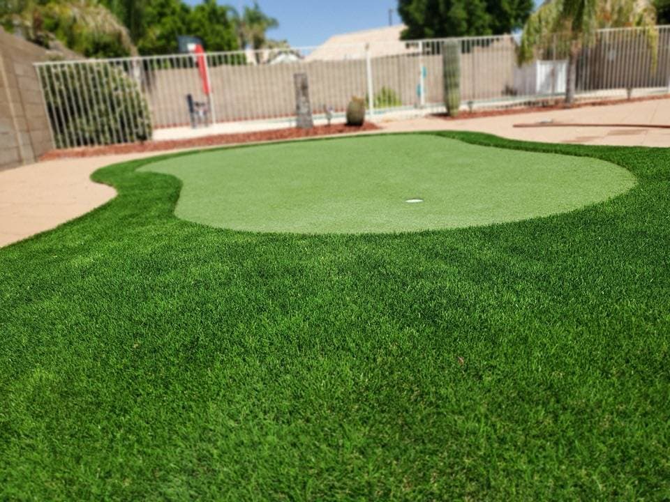 Lush green synthetic putting green in a residential backyard with manicured grass.