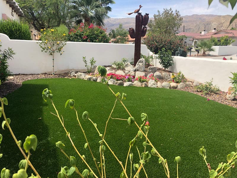 Desert landscape with artificial turf, cactus sculpture, and colorful flowering plants.