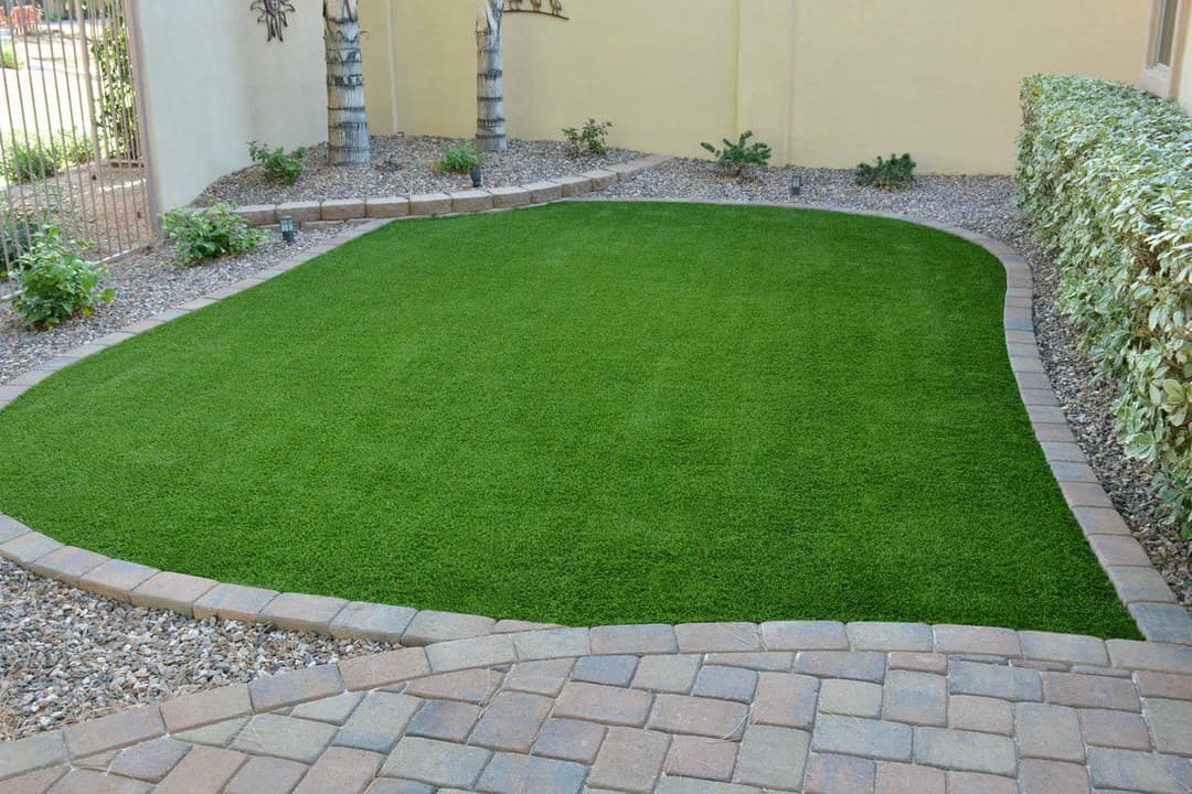 Lush green artificial turf lawn bordered by stone pathway and decorative plants.