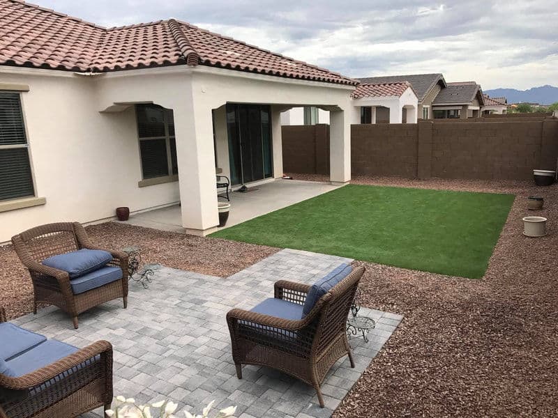 Modern backyard with artificial grass, paver patio, and two wicker chairs for outdoor relaxation.