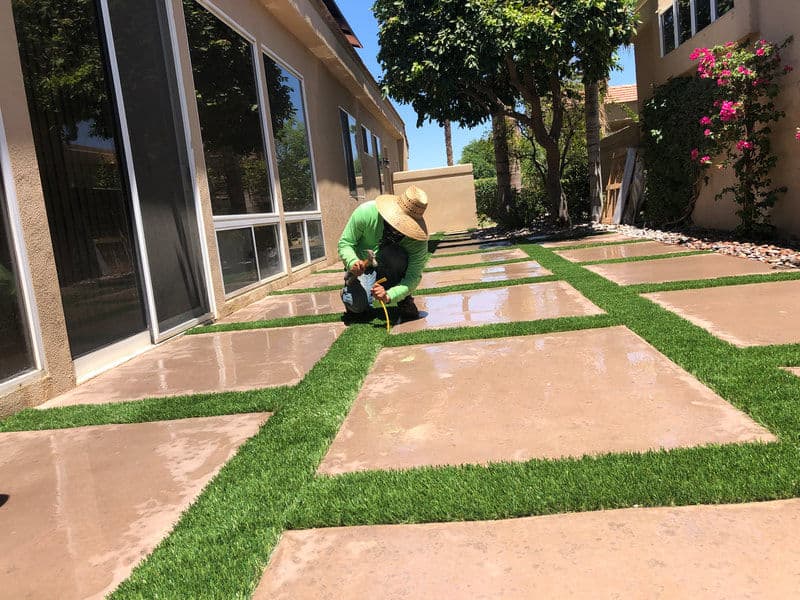 Landscaper installing artificial grass between concrete pavers in a residential yard.