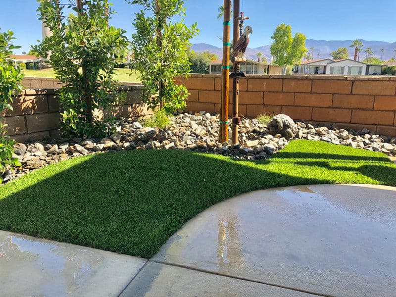 Lush green artificial turf with decorative stones and plants in a sunny outdoor setting.
