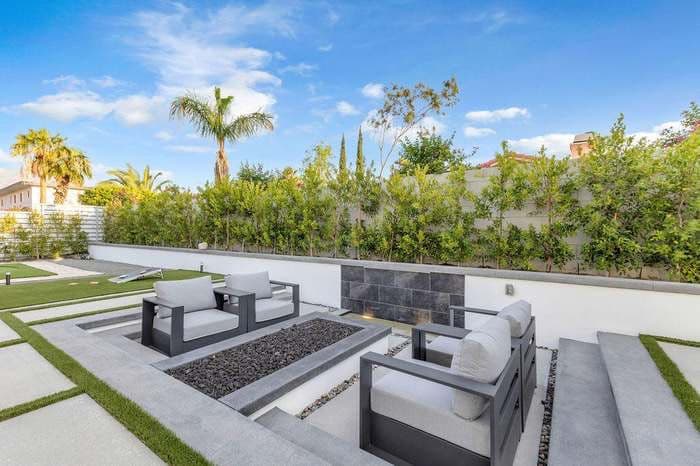 Modern outdoor lounge area with seating, landscaping, and palm trees under a blue sky.