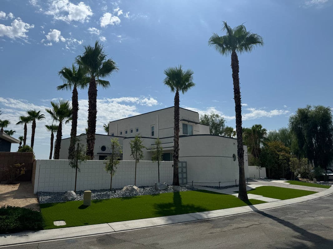 Modern white house surrounded by palm trees and green lawn under a blue sky.