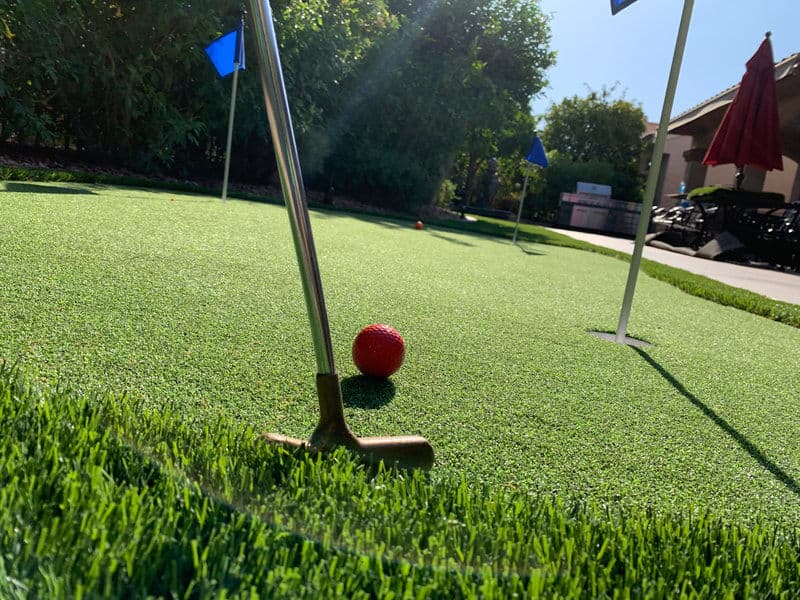Golf putting green with a red ball near the hole, surrounded by lush artificial grass.