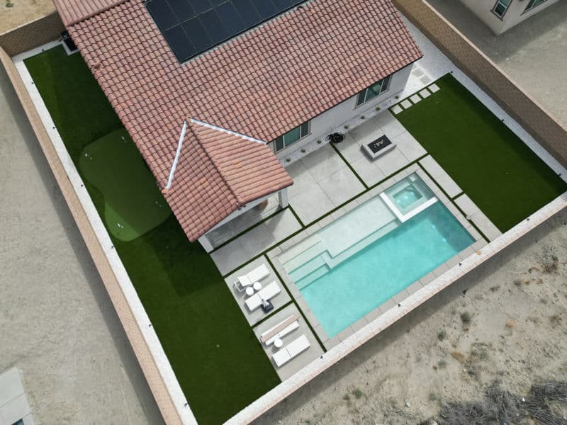 Aerial view of a modern home with a pool, patio, and landscaped yard featuring solar panels.