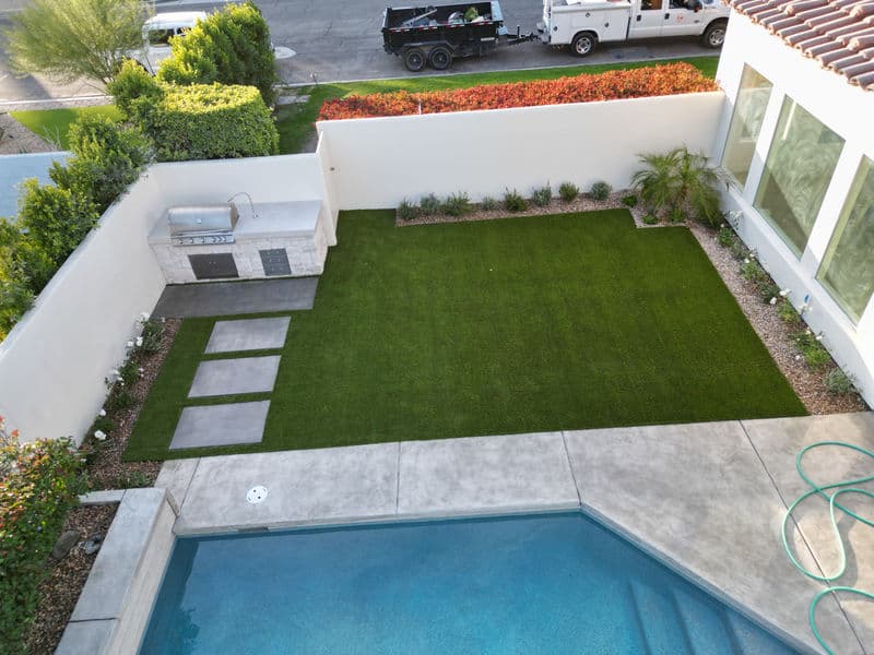 Aerial view of a modern backyard with synthetic turf, pool, patio, and outdoor grill station.
